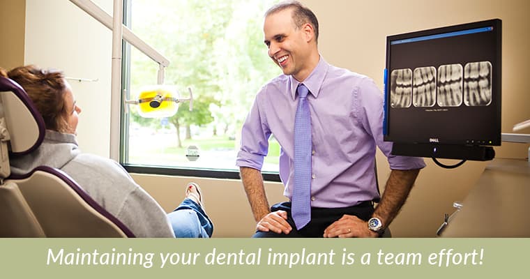 Dr. da Costa with a patient explaining how to care for a dental implant and text "Maintaining your dental implant is a team effort."