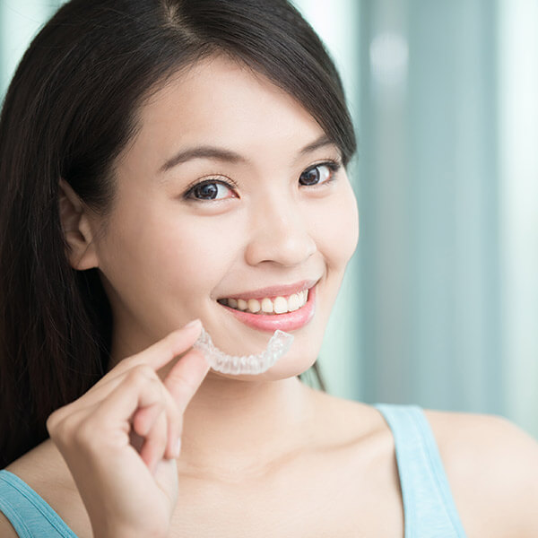 A woman showing holding clear aligners in front of her face
