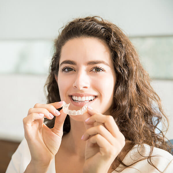 A woman smiling with aligners in her hands